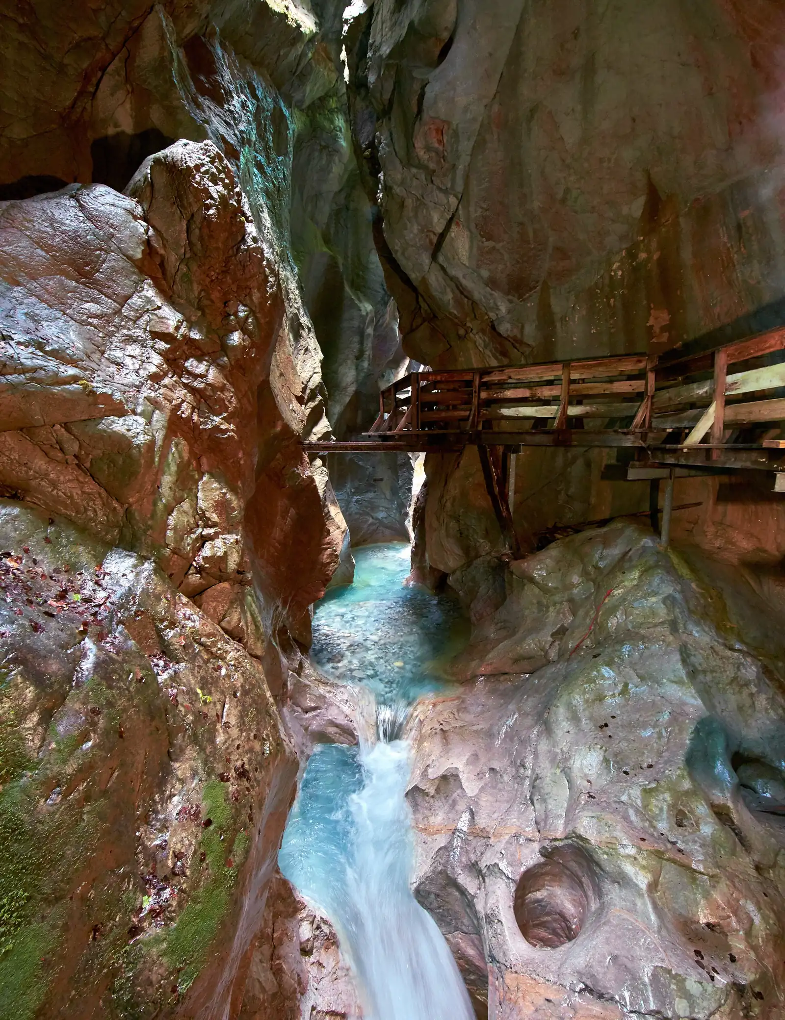 Holzsteg zwischen rötlichen Felswänden über türkisem Wasser in der Seisenbergklamm